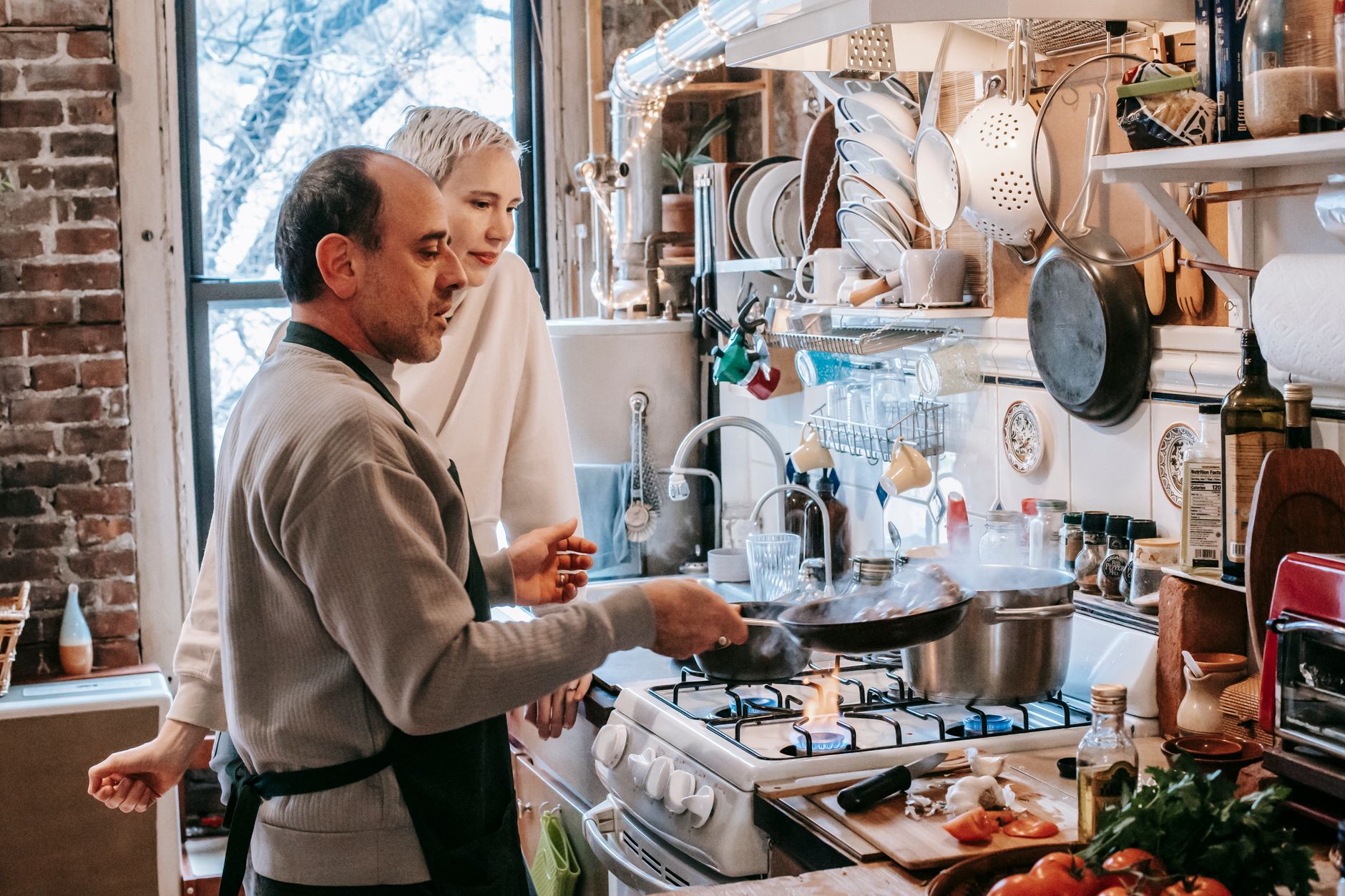 Man staat aan het fornuis en kookt samen met zijn vrouw in de keuken